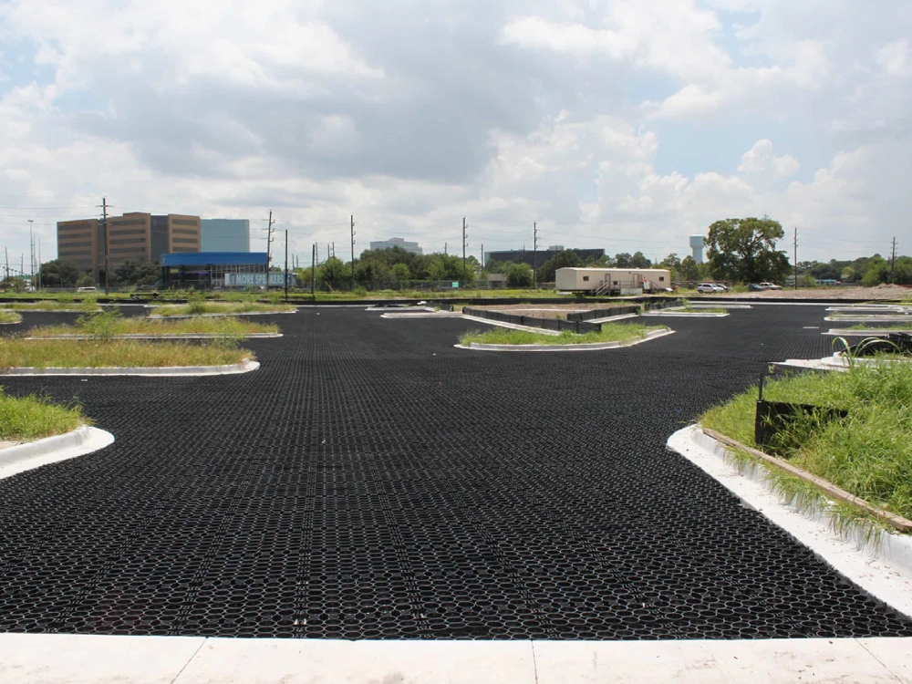 A large parking lot with black asphalt and grass.
